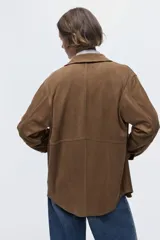 Camisa de manga larga en tejido con acabado tipo gamuza, de corte holgado con cuello clásico, cierre frontal de botones y puños abotonados. Presenta costuras decorativas visibles y bajo redondeado.