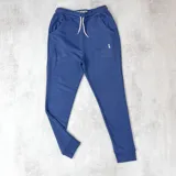 Pantalón de jogging azul con puños elásticos en los tobillos, cintura elástica con cordón ajustable y bolsillos laterales. Presenta un pequeño logo bordado en blanco en el muslo. Confeccionado en algodón sin felpa.