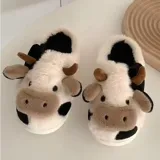 Pantuflas de peluche con diseño de vaca, confeccionadas en piel sintética suave. Cuentan con suela de goma antideslizante y diseño abierto en el talón.