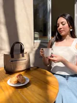 Cartera tipo tote de cuero color beige, con doble asa corta marrón y cierre superior con cremallera. Tiene un bolsillo frontal con cremallera y forro interior de tela con un bolsillo.