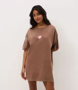 Camisón corto de algodón con efecto desteñido (acid wash), cuello redondo y mangas cortas. Presenta un pequeño estampado frontal de corazón en tono rosado con texto debajo.