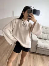 Polerón de cuello alto en color rosa suave, con diseño de calce holgado y mangas amplias. Presenta una textura acanalada fina y un corte relajado que aporta movimiento.