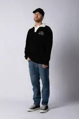 Sweater de punto con textura waffle en color blanco, con cuello polo en contraste color verde oscuro y cierre frontal de botones. Presenta un bordado decorativo en el pecho y un corte relajado.