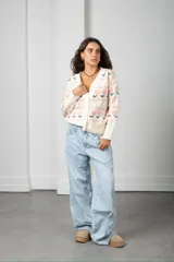 Cárdigan tejido de punto en color beige con diseño de flores y guardas caladas. Presenta escote en V, cierre frontal con botones y terminaciones acanaladas en puños y ruedo.