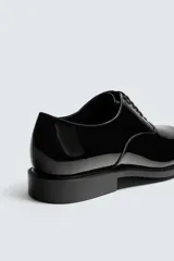 Zapato de vestir tipo derby color negro acharolado, con horma en punta y suela con ligero tacón.