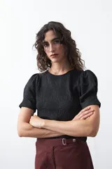 Remera negra de manga corta con textura floral en relieve. Presenta un diseño de inspiración romántica con mangas ligeramente abullonadas que aportan estructura y un ajuste al cuerpo.