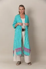 Túnica larga estampada en tonos turquesa, blanco y fucsia, con mangas cortas, calce holgado, tajos laterales y detalle de guarda en el ruedo.