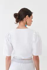 Top blanco tejido en hilado liviano con escote recto y mangas balloon de poplín 100% algodón. Tiene tiras tejidas para ajustar en la cintura.