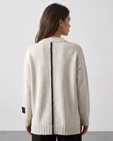Sweater oversized crudo de tejido de punto, con hombros caídos y mangas largas. Presenta líneas negras en contraste en los hombros, bordado artesanal con la frase "e pur si muove" en el frente y aberturas laterales en el dobladillo.