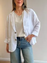 Blazer de lino color blanco, de corte relajado y líneas clásicas, con cuello de solapas y cierre frontal de dos botones.