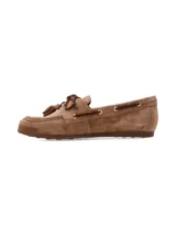 Mocasín náutico de cuero gamuza color camel, con detalles de costuras pespunteadas, cordones de cuero oscuro entrelazados con ojales metálicos dorados y borlas decorativas en el empeine.