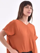 Blusa de corte holgado color naranja, con escote en V y mangas cortas tipo murciélago. Presenta una costura vertical central en el frente y una textura sutilmente arrugada.