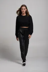Pantalón negro de cuero sintético con bolsillos laterales y botones metálicos a presión en los laterales.