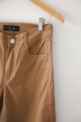 Pantalón de jean color café con corte recto, tiro alto, bolsillos delanteros y traseros, y tajos laterales en el ruedo. Presenta una franja vertical bordada en color rosa a lo largo de la costura lateral.