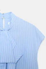 Camisa sin mangas confeccionada en algodón, con cuello redondo y detalle de lazada frontal. Presenta un diseño de corte holgado con bajo redondeado y cierre posterior mediante abertura y botones.