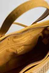 Cartera tipo tote color amarillo con detalles en textura tejida en la parte frontal y trasera, asas de mano y correa de hombro ajustable y desmontable. Incluye aplique metálico con el logo de la marca.