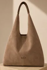Bolso tipo hobo grande confeccionado en cuero vacuno color marrón, con costura central vertical y placa metálica con el logo de la marca Pecarí.