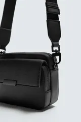 Bandolera negra con textura grabada, compartimento principal con cierre de cremallera y bolsillo interior con cremallera. Bolsillo frontal con solapa y cremallera. Asa de hombro removible y ajustable.