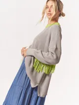 Buzo tejido oversized con bloques de color blanco y gris, cuello redondo en verde neón, tajos laterales y flecos verdes en las mangas.