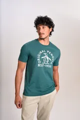Remera de algodón color verde petróleo con cuello redondo y mangas cortas. Presenta un estampado gráfico frontal en color blanco con el logo de la marca y la leyenda Original Penguin Est. 1955.