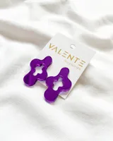 Par de aros colgantes de acrílico color violeta con forma geométrica irregular con aberturas.