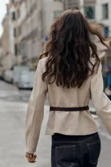 Blazer de cuello redondo y manga larga, confeccionado en tejido efecto ante. Presenta cierre frontal con botones, bolsillos con tapeta en el pecho y cinturón ajustable en la cintura.