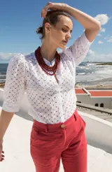 Camisa de estilo romántico confeccionada en tela broderie blanca, con mangas al codo abullonadas y cierre frontal con botones.