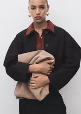 Chaqueta corta de corte recto con cuello camisero, cierre frontal de botones y dos bolsillos de parche laterales. Presenta mangas largas y forro interior.