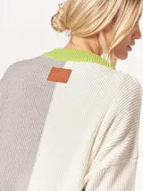 Buzo tejido oversized con bloques de color blanco y gris, cuello redondo en verde neón, tajos laterales y flecos verdes en las mangas.