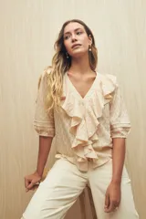 Blusa color crema con diseño calado, escote en V y volados frontales. Tiene mangas 3/4 con puños elastizados y cierre frontal con botones.