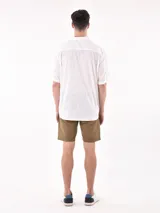 Camisa de manga corta color blanco roto con textura de tejido de lino o similar, corte holgado y cuello camisero.