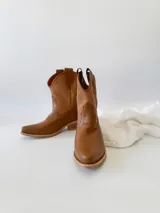 Botas texanas de cuero color camel, con caña media, punta fina y tiradores laterales.