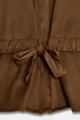 Camisa de estilo safari en color marrón con efecto ante, cuello subido y mangas anchas de largo tres cuartos con terminación en vuelta. Presenta bolsillos con solapa en el pecho, cintura ajustable con lazo del mismo tejido y cierre frontal oculto con cremallera y botones a presión.