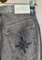 Jean de corte recto y largo, de tiro medio, color gris oscuro con efecto lavado. Presenta un bordado de estrella en los bolsillos traseros.