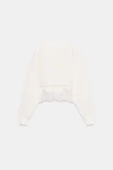 Sudadera crop de cuello redondo y manga larga con puños elásticos. Presenta un diseño de doble capa con un top interior satinado y un bajo decorado con encaje a tono.