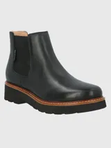 Botin tipo Chelsea de cuero negro con paneles laterales elásticos y detalle de textura en el talón. Cuenta con una suela de plataforma dentada en color negro con una franja intermedia en tono madera.