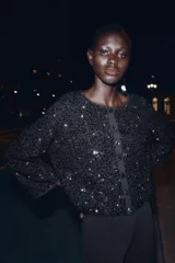 Chaqueta de punto negra con lentejuelas brillantes, cuello redondo, manga larga y cierre frontal con botones.