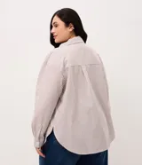 Camisa plus size alargada de Ashua, confeccionada en tela anarruga con diseño a rayas en tonos marrón y blanco. Presenta cuello inglés, cierre frontal con botones y mangas largas.