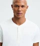 Remera masculina blanca de manga corta, con cuello redondo y abertura frontal con botones. Confeccionada en algodón y poliéster con textura, de corte ajustado.