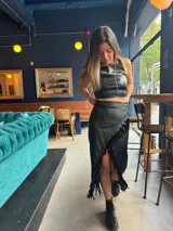Pollera midi negra de cuero sintético con abertura frontal y flecos largos en el ruedo. Se combina con un crop top haciendo juego y botas de caña baja.