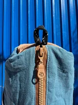 Necessaire azul y marrón con grifa de goma, detalles de cordón, cierre y bolsillo transparente interior.