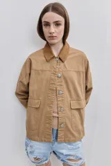 Campera de gabardina tostada, con cuello camisero de pana marrón, cierre frontal de botones metálicos y bolsillos delanteros aplicados con solapa.