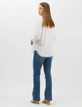Camisa de tencel color blanco, con cuello camisero, cierre frontal de botones y dos bolsillos en el pecho. Presenta mangas largas con presilla para regular el largo y ruedo con detalle de flecos.