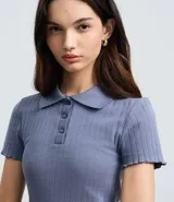 Blusa de punto acanalado color azul, con cuello polo, cierre frontal de botones y mangas cortas con terminación tipo frufru.