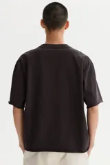 Remera boxy de algodón en punto liviano, de color negro, con hombros caídos, cuello redondo acanalado y corte oversized.