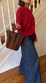 Matera de cuero con diseño de paneles verticales en combinación de colores azul, verde, marrón y bordó. Cuenta con dos asas cortas de cuero y estructura rígida.