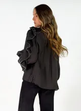 Blusa blanca de corte holgado con volados en el frente y en las mangas. Presenta un delicado borde festoneado en color negro en los volados y puños con elástico.