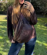 Riñonera de tamaño XL en color marrón chocolate, con diseño exterior trenzado y un parche frontal con monograma grabado. Cuenta con cierre diagonal y correa regulable.