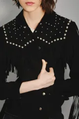 Camisa negra de gamuza caprina con cuello y hombros adornados con tachas metálicas plateadas. Presenta flecos decorativos en el canesú y botones plateados en el frente.