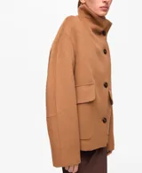 Abrigo corto de paño en color camel, con cuello alto, cierre frontal de botones y bolsillos laterales con solapa. Presenta un diseño de corte recto y estructura holgada.